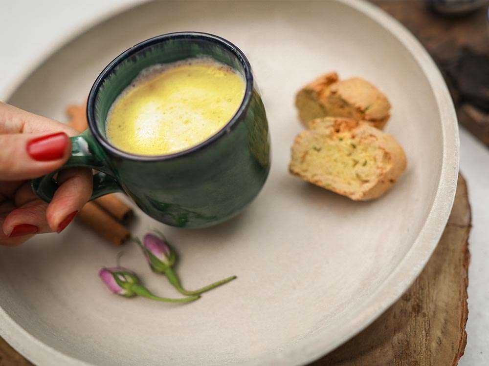 Saffron chai latte in a pale cup with cinnamon, cardamom and saffron threads