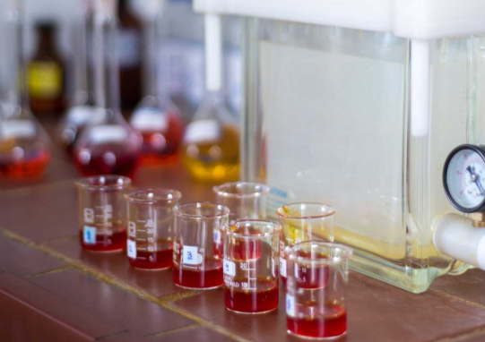 Laboratory beakers containing red liquid beside scientific equipment