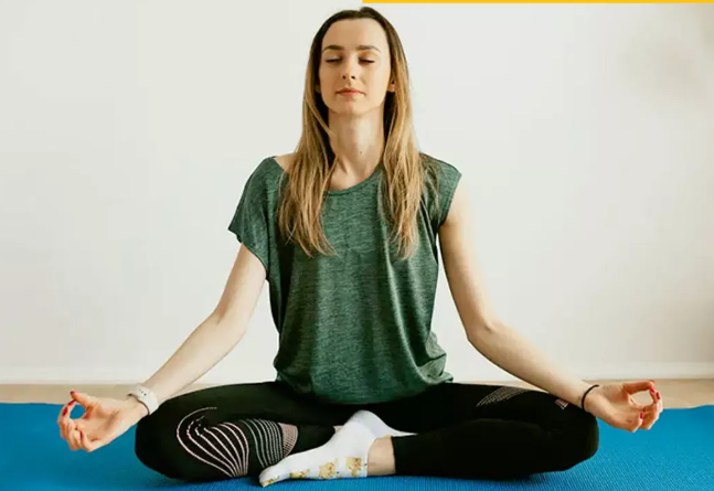 Woman sitting cross-legged on a yoga mat with her eyes closed
