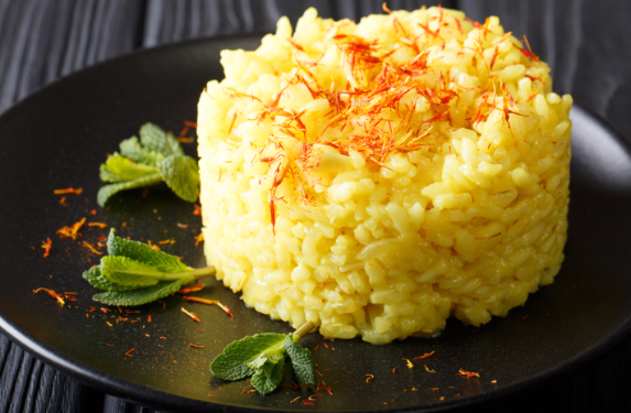 „Safranrisotto – italienisches Risotto alla Milanese mit goldgelber Farbe, cremiger Textur und Parmesanflocken auf dunklem Teller.“