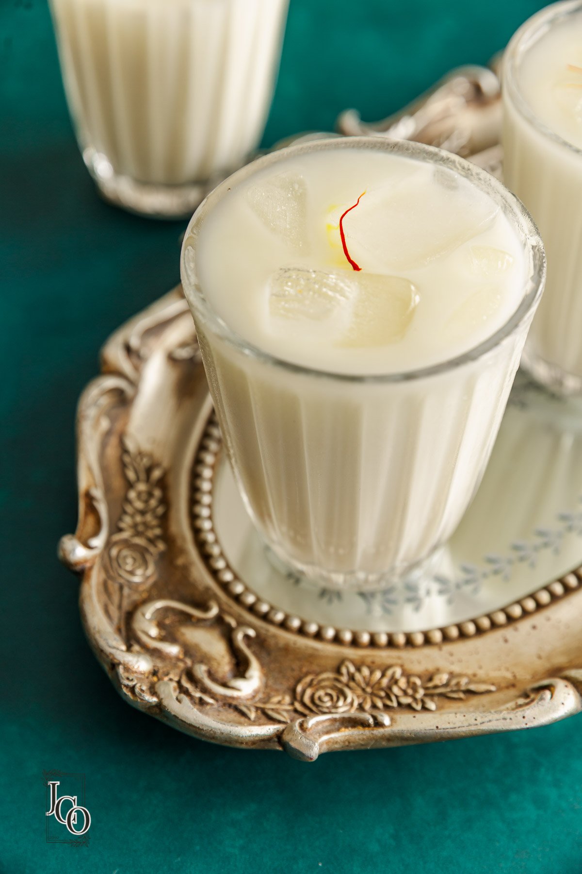 Glas mit kalter Safran-Kardamom-Horchata, verziert mit Zimtstange und goldenen Safranfäden auf Eisklötzen.