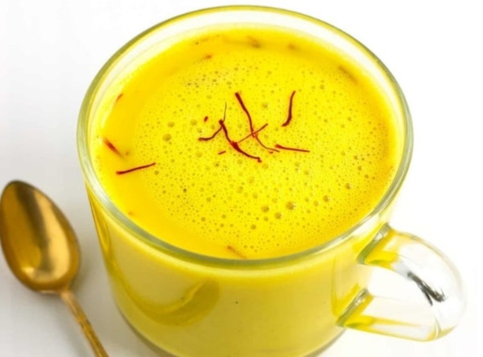 Warme Kesar Doodh in einer Keramiktasse, indische Safranmilch mit goldgelber Farbe, verfeinert mit Safranfäden als traditionelles Abendgetränk.
