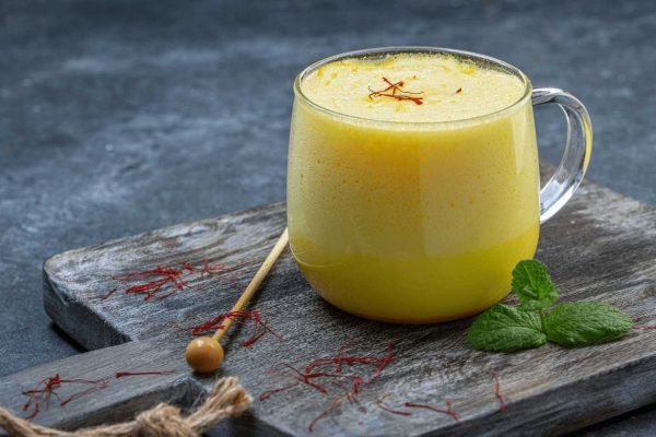 Warme Safran Milch in einer Keramiktasse mit goldgelber Farbe, zubereitet aus leicht zerstoßenen Safranfäden als ruhiges Abendritual.