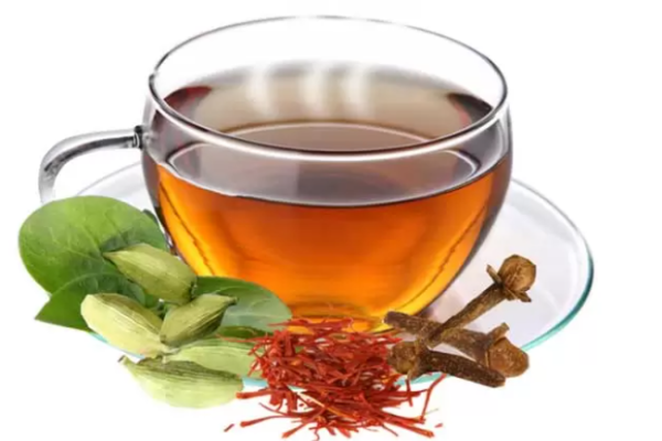 Safran Tee mit Gewürzen in einer Tasse, goldgelbe Farbe mit Safranfäden, Zimtstange und Kardamom als wärmendes Wintergetränk.