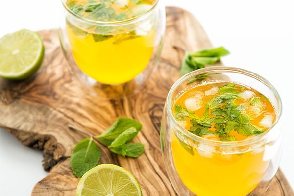 Safran Zitronenwasser in einem Glas mit hellgoldener Farbe, mit Zitronenscheibe und Eiswürfeln als erfrischendes Sommergetränk.